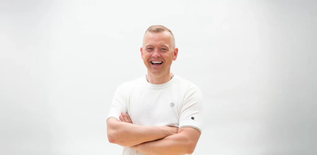 Tom Haver met gekruiste armen, poserend voor een witte achtergrond.