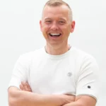 Tom Haver met korte coupe en wit T-shirt met opgerolde armen tegen een witte achtergrond.