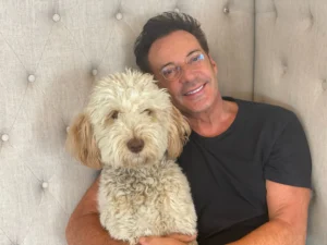 Gerard Joling zit thuis op de bank en knuffelt zijn hond Buddy.