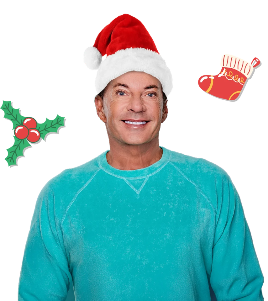 Gerard Joling met een kerstmanmuts en turquoise trui, omringd door kerstdecoraties.