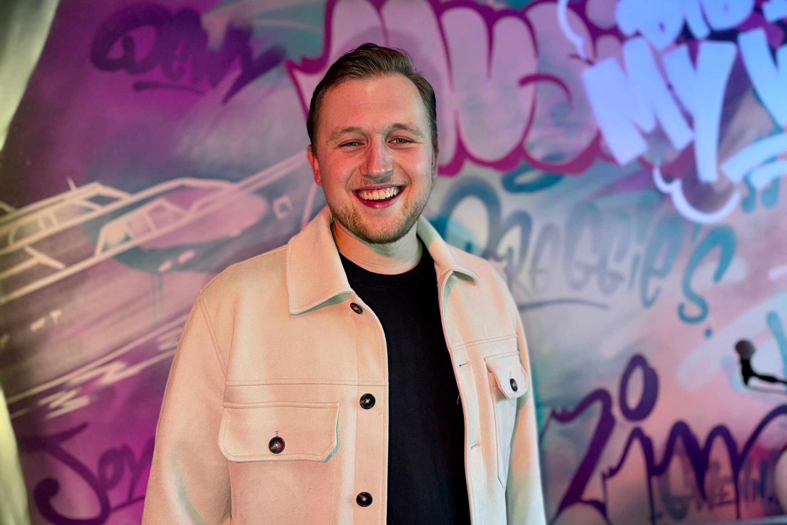 Teun Landzaat lacht tijdens een repetitie in de studio met kleurrijke graffiti op de achtergrond.