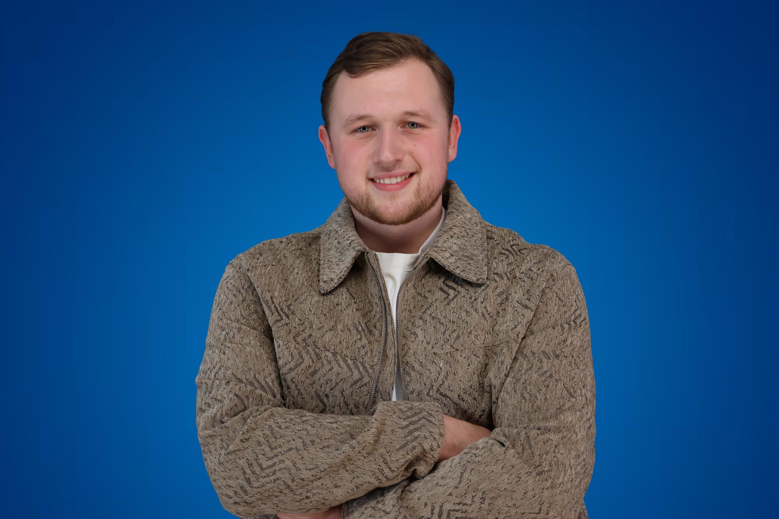 Teun Landzaat poseert met een glimlach en gekruiste armen voor een effen blauwe achtergrond.