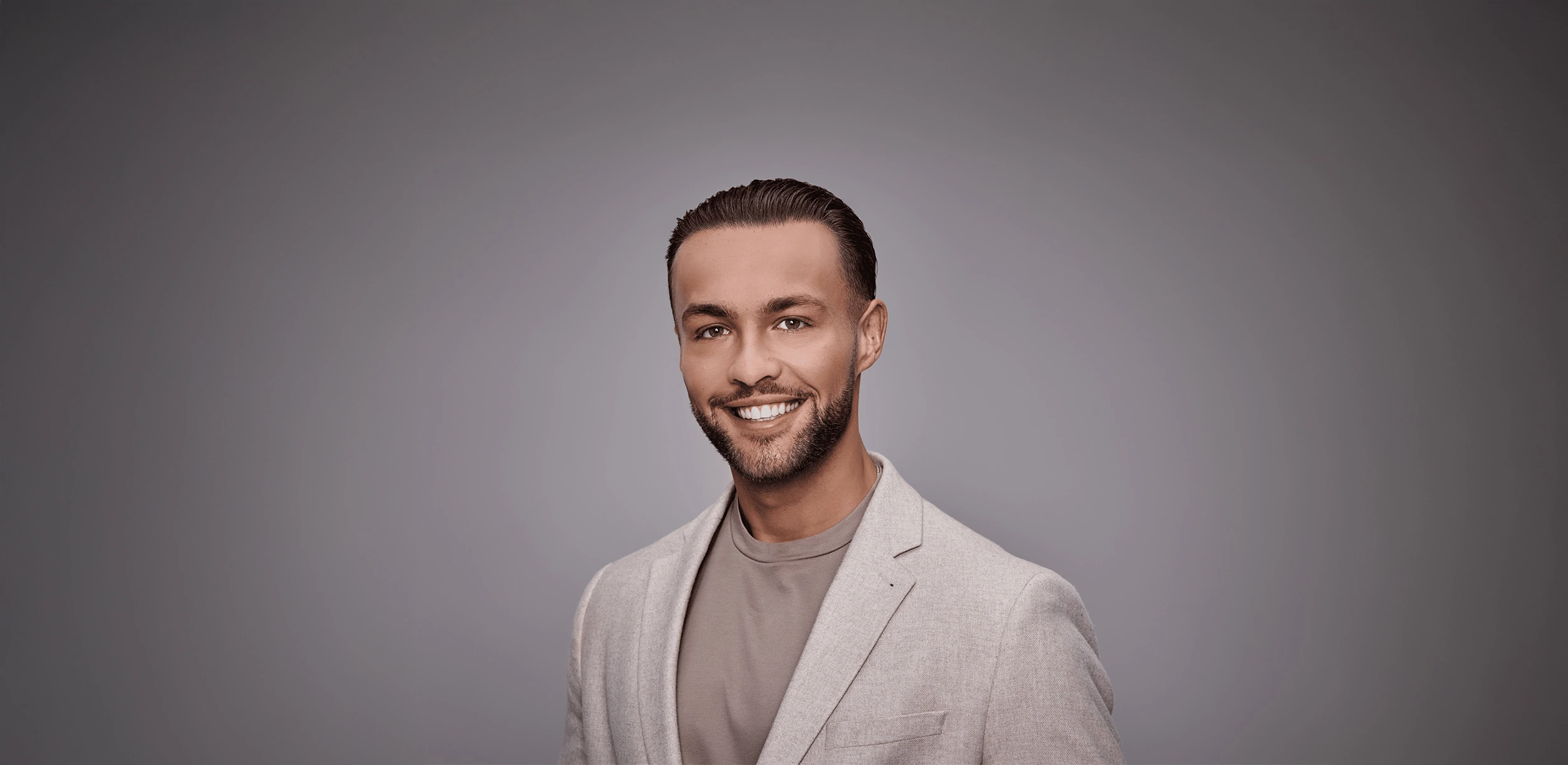 Portret van Delano Duncker in een lichtgrijs colbert tegen een grijze achtergrond.