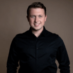 Teun Landzaat met kort bruin haar en een zwarte blouse poseert lachend voor een neutrale bruine achtergrond.