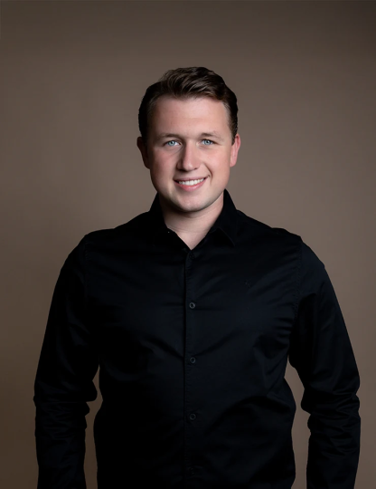 Teun Landzaat met kort bruin haar en een zwarte blouse poseert lachend voor een neutrale bruine achtergrond.