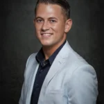 Portret van Menno Aben in een lichtblauw colbert en donker overhemd voor een donkere achtergrond.