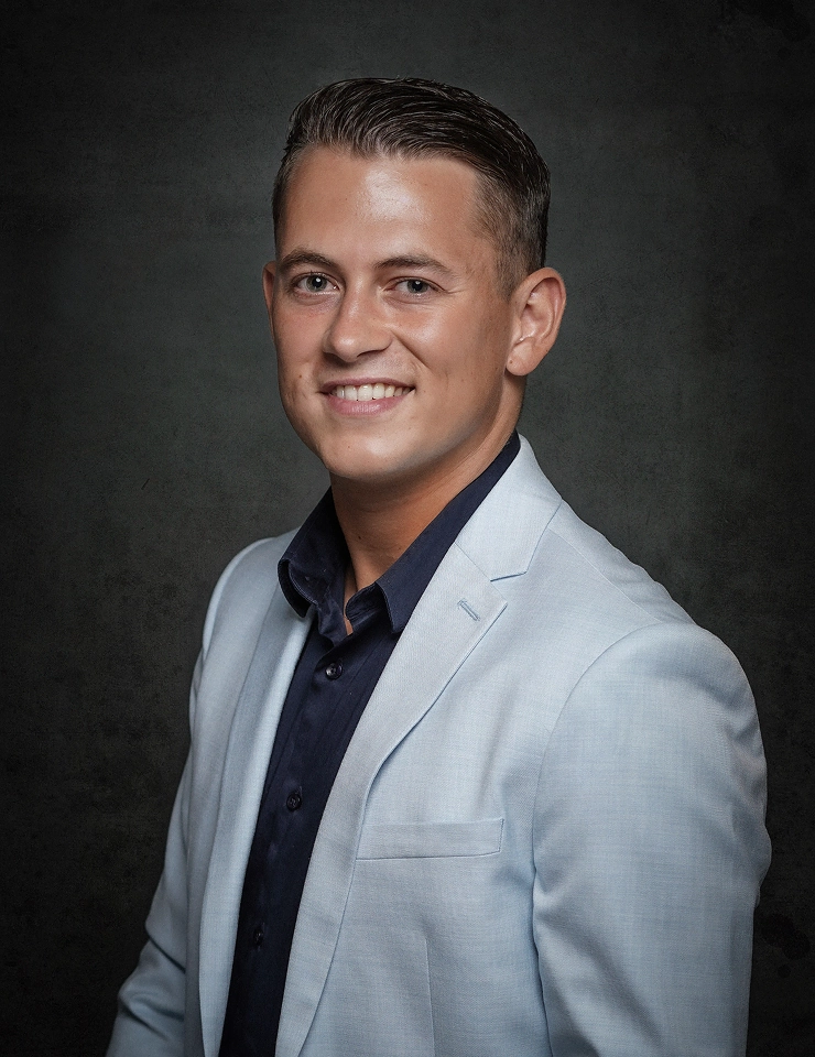 Portret van Menno Aben in een lichtblauw colbert en donker overhemd voor een donkere achtergrond.