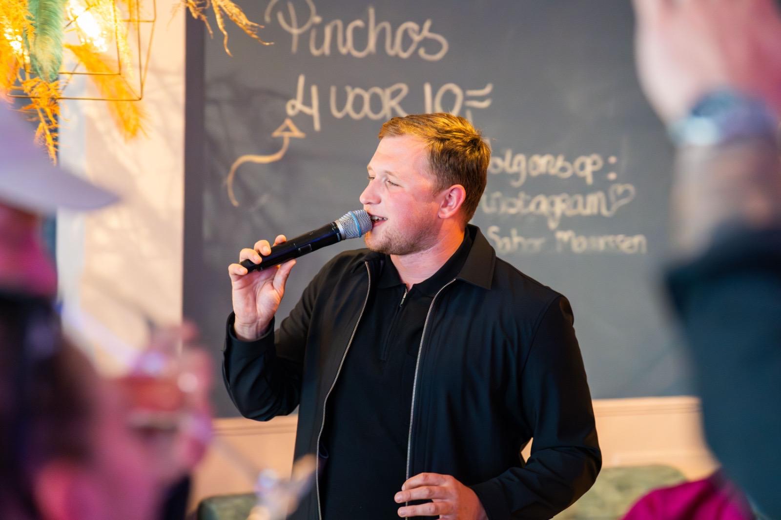 Teun Landzaat zingt met een microfoon tijdens een optreden in een gezellige horecagelegenheid.