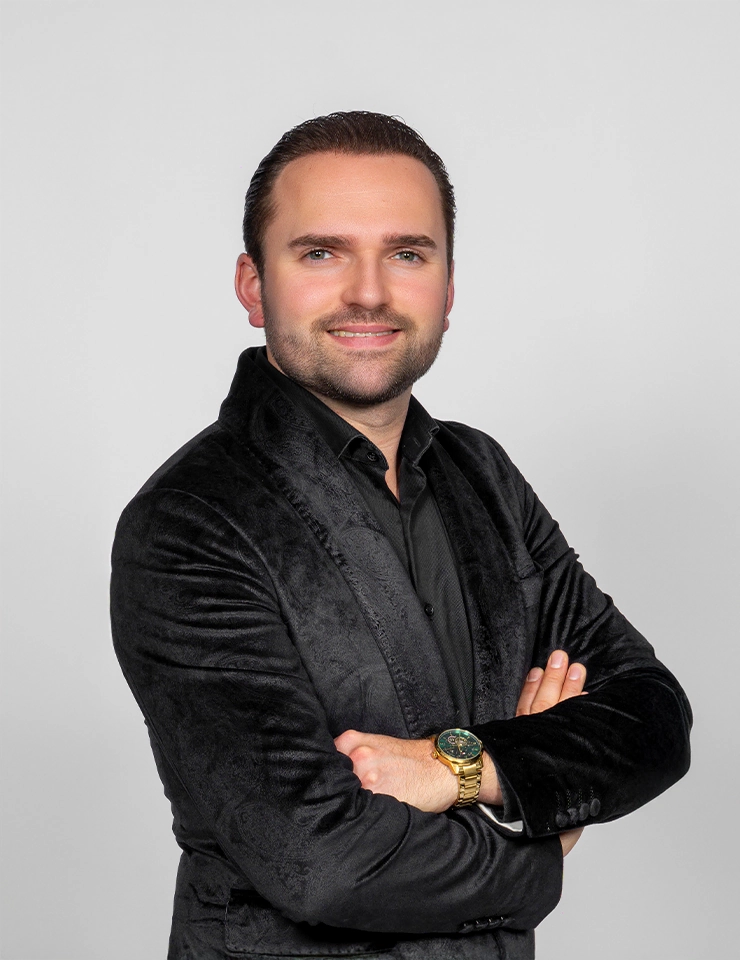 Bryan Stricker met kort haar en een zwarte blouse met colbert poseert lachend voor een neutrale witte achtergrond.